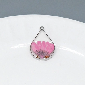 Macro shot of teardrop resin pendant with real pink dried flower and gold foil flakes