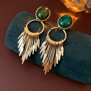 Macro detail of gold vintage earrings with green oval gemstone and long metallic tassels