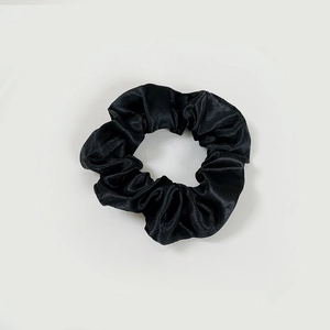 Macro shot of black satin scrunchie showing smooth texture and elastic pleats detail