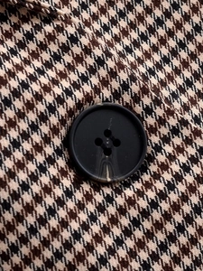 Détail de la texture pied-de-poule et d'un bouton noir mat à quatre trous sur un blazer