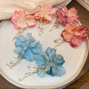 Detail of floral earrings with fabric petals and pearl tassels on a white ceramic tray