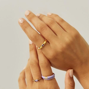 Elegant gold rings set with purple gemstones and enamel on hand with a warm background