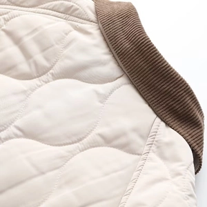 Detail view of quilted cream-white fabric with a contrast brown ribbed collar and stitching