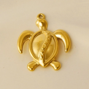 Macro shot of a polished gold stainless steel sea turtle pendant on a beige surface