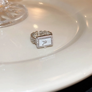 Macro detail of a silver watch-style ring with white shell dial and zircon inlay