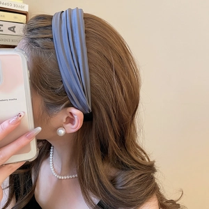 Détail d'un serre-tête en tissu plissé bleu porté avec des bijoux en perles élégants