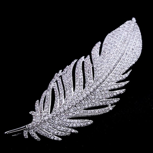 Detailed close-up of a silver feather brooch with sparkling zircons on black background