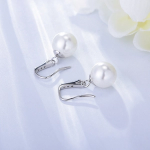 Detailed close-up of 925 silver pearl drop earrings on light blue silk fabric