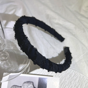 Close-up of black fabric sponge headband with frayed edges on white pleated cloth