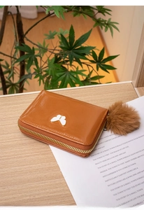 Brown oil leather wallet with butterfly ornament and pompom charm on a natural background