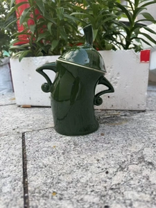 Detailed close-up of a dark green anthropomorphic ceramic canister with arm-shaped handles