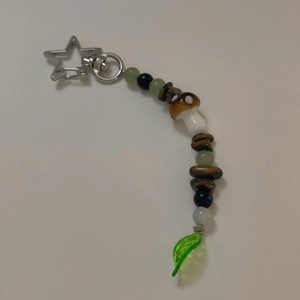 Dettaglio di un portachiavi a perline fatto a mano con fungo e ciondolo a foglia verde