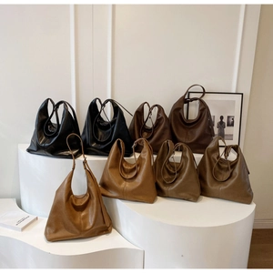Three minimalist soft leather tote bags in black, dark brown, and caramel on a white stand