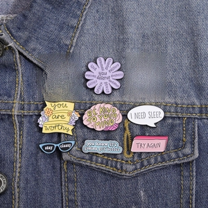 Close-up of nine creative enamel pins with English quotes on a blue denim jacket