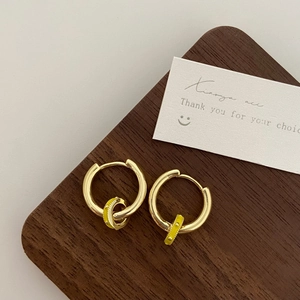 Close-up of golden hoop earrings with yellow enamel pendants on a wooden board