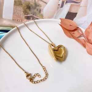 Polished gold heart locket necklace with openable pendant on white porcelain dish