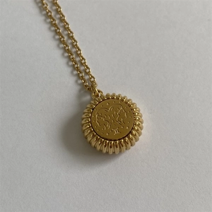 Macro detail of gold Gemini pendant featuring zodiac sign and Roman numeral II engraving