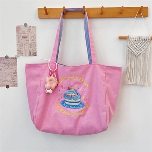 Close-up of pink canvas tote with cake embroidery and checkered strap detail