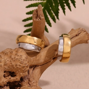 Close-up of wide two-tone C-shape hoop earrings on natural wood with leaves