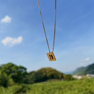 Detail of gold titanium steel necklace featuring a square pendant with cutout letter N