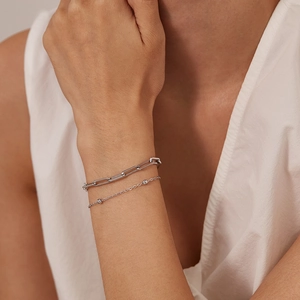 Close-up of a layered silver paperclip chain and bead bracelet on a model wrist