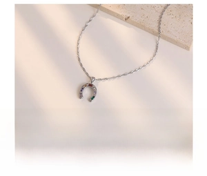 Detailed macro of silver horseshoe necklace with colorful zircon stones on beige stone
