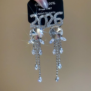 Détail de boucles d'oreilles pendantes avec chiffre 2026 brillant et cristaux argentés