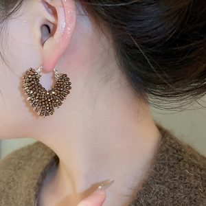 Close-up of heart-shaped crystal beaded hoop earrings worn by a model in warm light