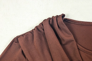 Detailed view of the dark brown knitted fabric showing pleated shoulder and round neckline