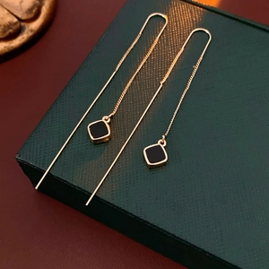 Dettaglio di lunghi orecchini a nappa dorati con pietre preziose quadrate nere minimaliste