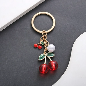 Close-up of golden keychain with red cherry charms and a white pearl on a split background