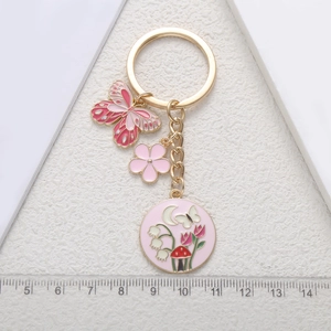 Pink enamel flower and butterfly keychain with gold chain and circular charms on white background