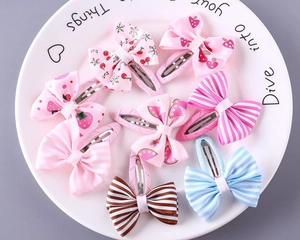 Flat lay of eight colorful striped bow hair clips with fruit patterns on a white plate