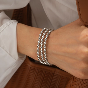 Dettaglio del bracciale rigido a tre strati di perle argentate indossato sul polso chic