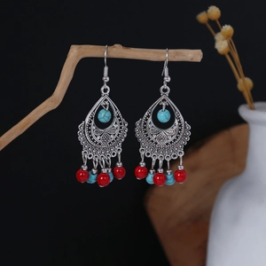 Artistic close-up of Bohemian oval earrings with turquoise and red beads on dry branches