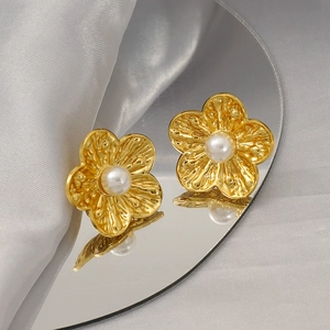 Vintage gold plated flower stud earrings with textured petals and center pearl on mirror