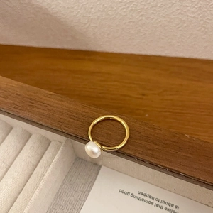 Close-up of minimalist gold ring with white pearl detail on rustic wooden surface