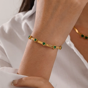 Elegant gold snake chain bracelet featuring emerald green heart charms on a female model
