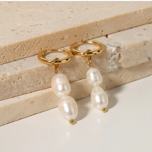 Close-up of gold titanium hoop earrings with two irregular freshwater pearls on beige tile