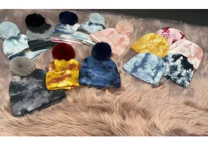 Detailed flat lay of colorful tie-dye knit beanies with faux fur pom-poms and ribbed cuffs
