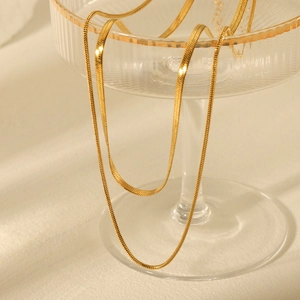 Double-layered gold flat snake chain necklace draped inside a luxury crystal glass