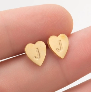 Vue macro d'une boucle d'oreille cœur dorée avec lettre J gravée tenue entre les doigts
