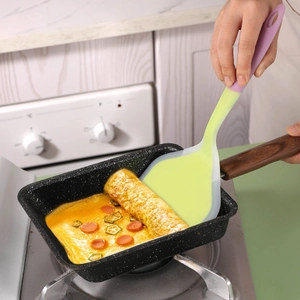 Spatule bicolore en silicone soulevant une omelette japonaise dans une poêle carrée
