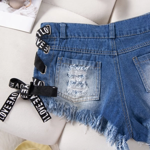 Dettaglio degli shorts in denim blu con nastro LOVE, strappi e orli sfilacciati