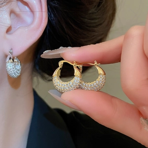 Detailed macro of C-shaped golden earrings with pavé zircon stones and secure clasp closure