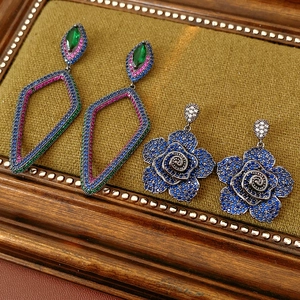 Detailed shot of vintage geometric drop earrings and blue rose studs on green velvet
