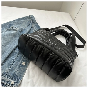 Dettaglio della borsa tote nera trapuntata in nylon con giacca di jeans su sfondo bianco