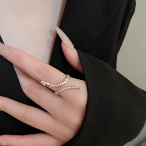 Detailed close-up of a gold snake-shaped ring on model's finger with a dark background