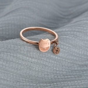 Nahaufnahme der roségoldenen Winkekatze-Ring mit Glücksmünze auf blauem Stoff