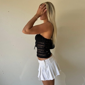 Detailed side view of a black lace camisole paired with a white pleated mini skirt